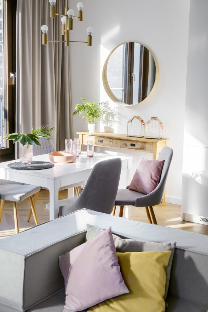 Nowoczesny salon z sofą, stołem jadalnym, krzesłami i okrągłym lustrem w słonecznym wnętrzu.