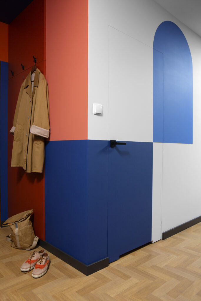 Nowoczesne wnętrze z beżowym płaszczem na wieszakach, trampkami na podłodze i dwukolorową niebieską szafką.